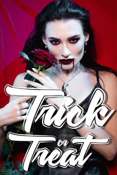 pale and brunette woman with blood on face holding rose near trick or treat lettering on red