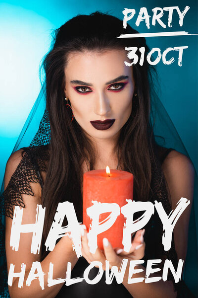 pale woman with black makeup and veil holding burning candle near happy halloween lettering on blue
