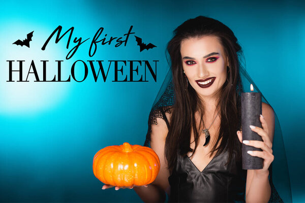 joyful woman with black makeup and veil holding burning candle and pumpkin near my first halloween lettering on blue