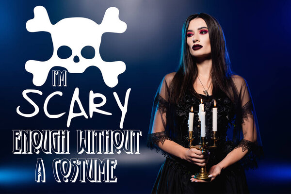 woman in black dress and veil holding burning candles near i am scary enough without a costume lettering on blue 