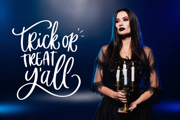 woman in black dress and veil holding burning candles near trick or treat lettering on blue 