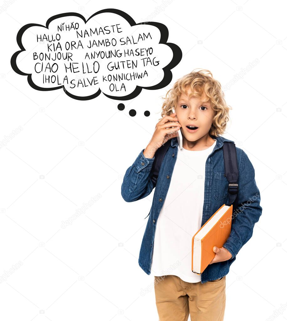 shocked and blonde schoolboy holding book and talking on smartphone near speech bubble with greeting words on white 