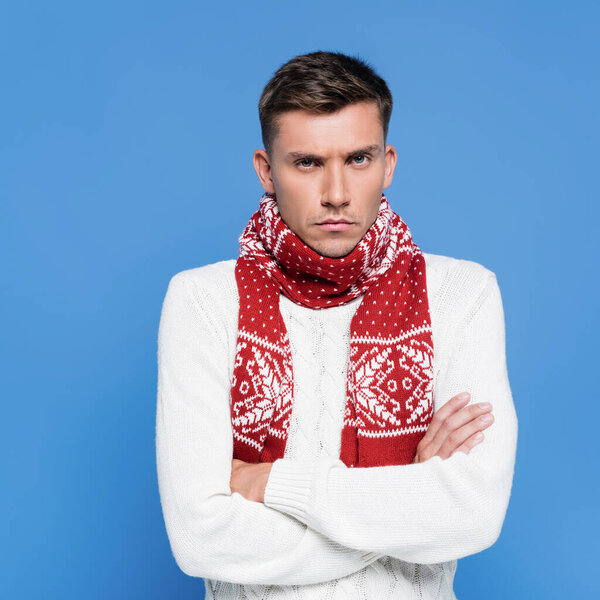 Портрет рассерженного молодого человека со скрещенными руками, смотрящего на камеру, изолированную на голубом