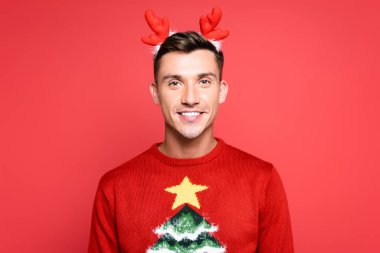 Front view of happy young adult man with hoop on head looking at camera isolated on red clipart