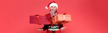 Noel Baba şapkalı neşeli adam kırmızı arka plana hediyeler atıyor. 