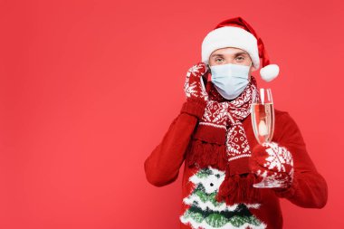 Noel Baba şapkalı ve tıbbi maskeli bir adam akıllı telefondan konuşuyor. Elinde kırmızı önplanda bulanık bir şampanya kadehi var. 