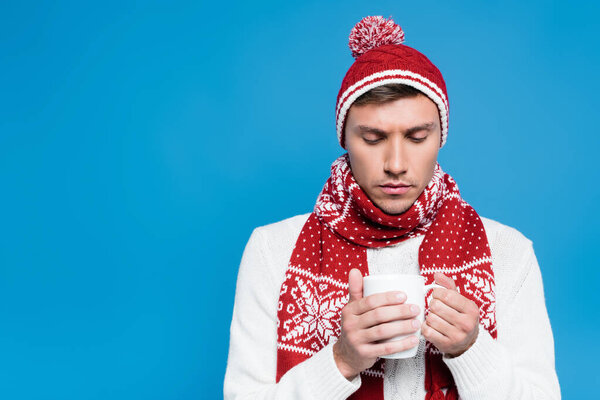 Больной молодой человек в трикотаже держит чашку изолированы на синий