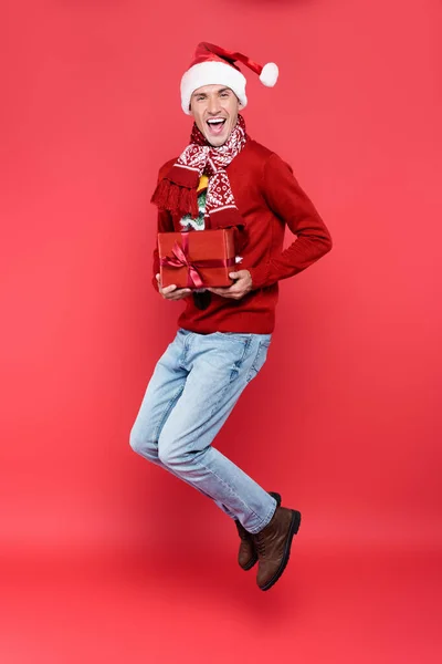 Wesoły Człowiek Kapeluszu Santa Trzymając Pudełko Prezentów Podczas Skakania Czerwonym — Zdjęcie stockowe
