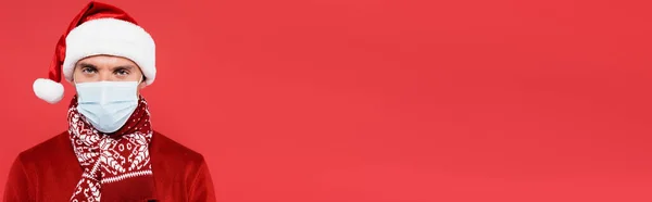 Человек Шляпе Санты Медицинской Маске Смотрит Камеру Изолированную Красном Баннер — стоковое фото