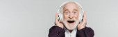 Nadšený starší muž poslouchá hudbu v bezdrátových sluchátkách izolovaných na šedé, banner 