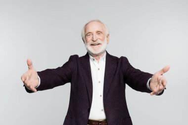 Gömlekli ve ceketli gülümseyen son sınıf öğrencisi gri önplanda bulanık ön planda kameraya el kaldırıyor. 
