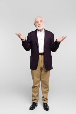Gri arka planda omuz silkme hareketi gösteren ceketli ve gömlekli kafası karışmış yaşlı adam. 