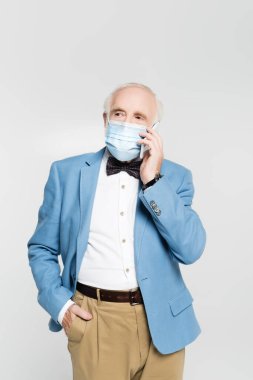 Tıbbi maskeli ve ceketli kıdemli bir adam gri telefonda akıllı telefondan konuşuyor. 