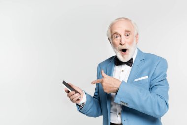 Excited senior man in bow tie and jacket pointing with finger at smartphone isolated on grey  clipart