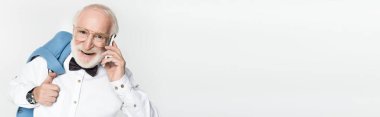Papyonlu gülümseyen yaşlı bir adam ceketini tutuyor ve akıllı telefonuyla konuşuyor. Gri, afişte izole bir şekilde. 