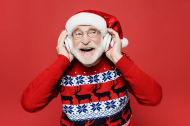 Noel Baba şapkalı, kazaklı, kulaklıklara dokunan son sınıf öğrencisi. Kırmızıda izole edilmiş.