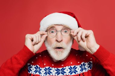 Şok olmuş son sınıf öğrencisi Noel Baba şapkası ve gözlükleriyle kırmızı kameraya bakıyor. 