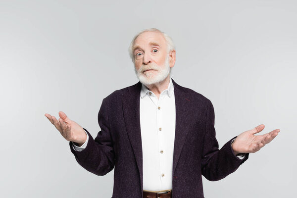 Confused senior man showing dubium gesture while looking at camera isolated on grey 