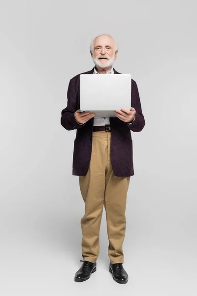 Starszy Mężczyzna Uśmiecha Się Kamery Trzymając Laptopa Szarym Tle — Zdjęcie stockowe