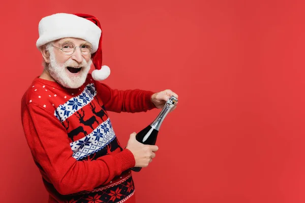 戴着圣诞礼帽的快乐的老人手里拿着一瓶香槟酒 是用红色隔开的 — 图库照片