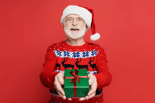 Lächelnder Älterer Herr Mit Weihnachtsmannmütze Zeigt Gegenwart Auf Verschwommenem Vordergrund — Stockfoto