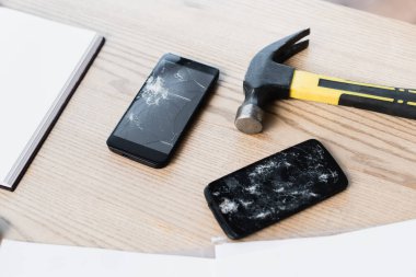 Smashed smartphones with hammer and blank notebook on textured wooden background clipart