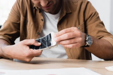 Cropped view of businessman disassemble smashed smartphone while sitting at table on blurred foreground clipart