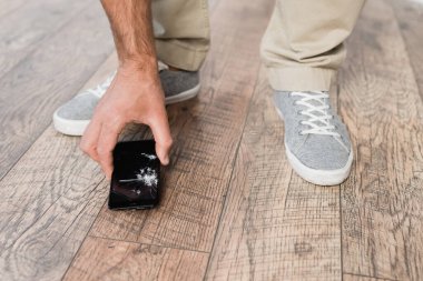 Cropped view of businessman taking smashed smartphone from floor clipart