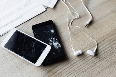 Top view of earphones and smashed smartphones near documents on wooden background, banner clipart
