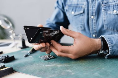 Bozuk akıllı telefonun parçalanmış parçalarının görüntüsünü iş yerindeki bulanık arkaplandaki tamircinin ellerinde kapat
