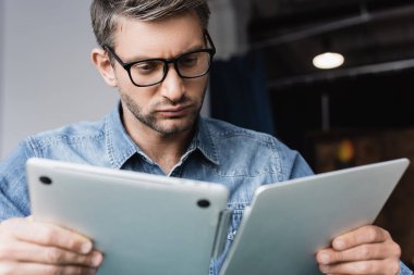 Gözlüklü odaklı tamirci bulanık önplandaki hasarlı laptopa bakıyor.