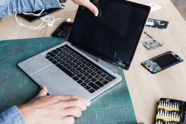 Hasarlı dizüstü bilgisayarı olan tamircinin iş yerinde parçalanmış cep telefonlarıyla boş ekranla görüntüsü kesilmiş.