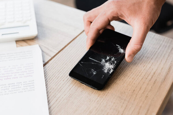 Cropped view of man putting smashed smartphone on table on blurred background