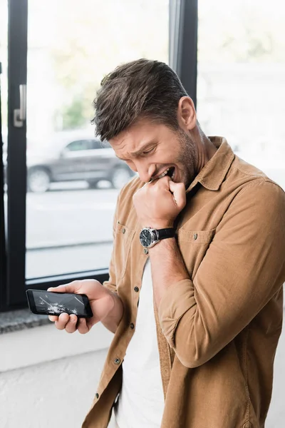 Frightened Businessman Biting Fist While Looking Smashed Smartphone Blurred Window — Stock Photo, Image