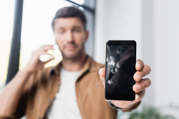 Smashed smartphone in hand of businessman on blurred background