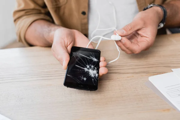 Vista Cortada Empresário Com Fone Ouvido Segurando Celular Esmagado Mesa — Fotografia de Stock