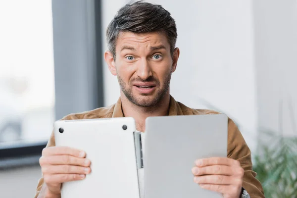 Confused Businessman Looking Camera While Holding Broken Laptop Blurred Background — Stock Photo, Image