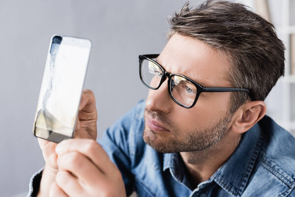 Focused repairman in eyeglasses looking at broken touchscreen in office
