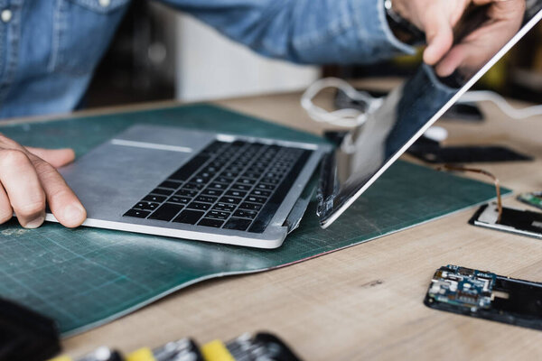 Cropped view of repairman holding damaged laptop at workplace on blurred background