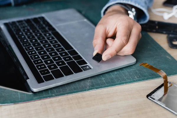 Cropped view of repairman holding broken key of laptop keyboard at workplace on blurred background