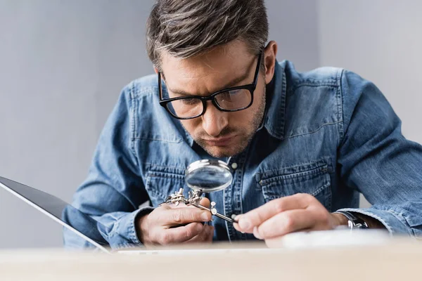 Focused Repairman Eyeglasses Magnifier Looking Broken Laptop Blurred Workplace Foreground — Stock Photo, Image