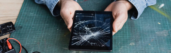 Cropped view of repairman holding smashed digital tablet at workplace, banner