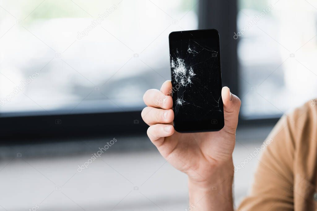 Cropped view of businessman holding damaged smartphone on blurred background