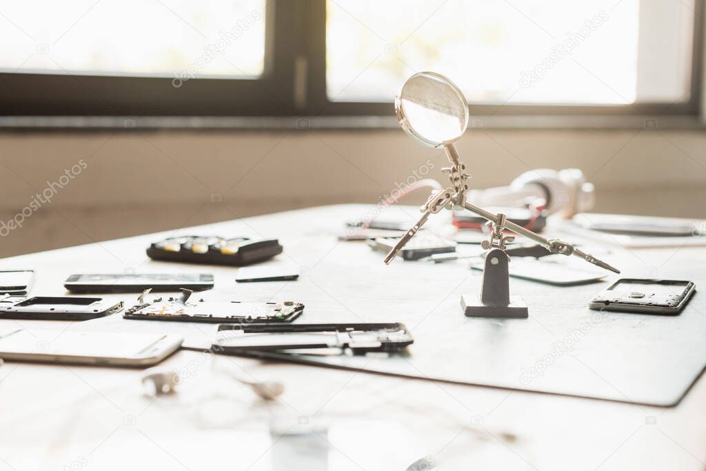 Disassembled parts of mobile phones with magnifier on table with blurred window on background