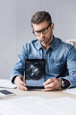 Parçalanmış dijital tabletli yorgun işadamı iş yerinde bulanık önplanda oturuyor
