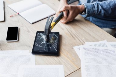 İş yerinde belgelerle otururken işadamının çekiçle dijital tablete vurduğu görüntüler