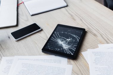 Dökümanların yanında parçalanmış dijital tablet ve ahşap arkaplanda dijital aygıtlar