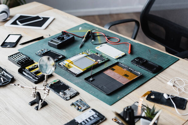 Flat lay of disassembled parts of devices, multi meter, screwdriver and magnifier on workplace