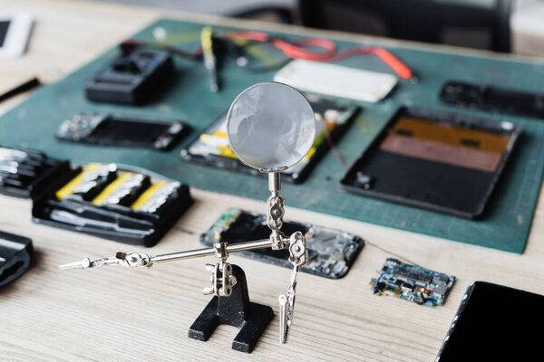 Flat lay of magnifier with disassembled parts of devices on workplace on blurred background