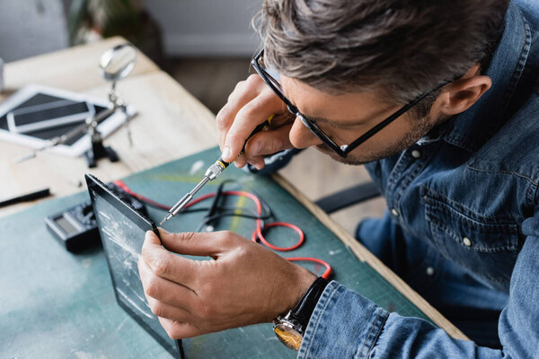 High angle view of repairman with screwdriver fixing smashed display of tablet at workplace on blurred background